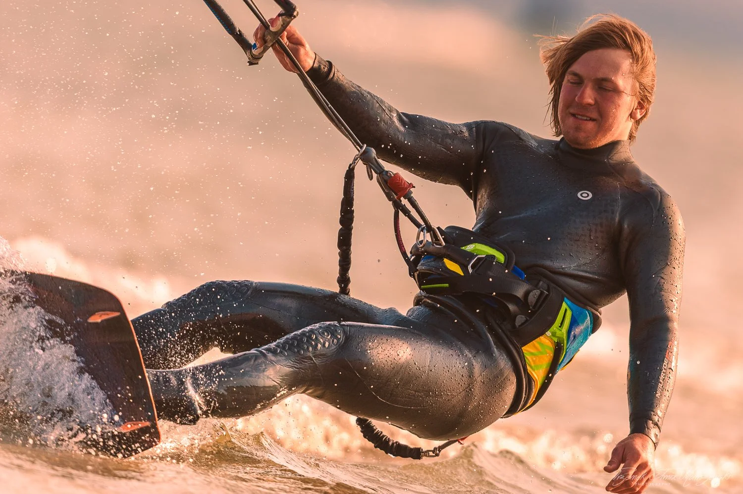 A man in a wetsuit water skiing on a lake during sunset, leaning back with a serious expression.