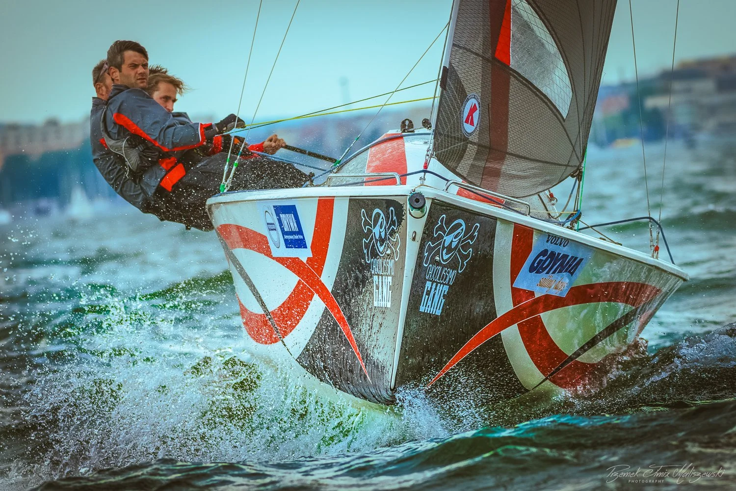 Two sailors on a racing sailboat leaning out over the water during a competition.