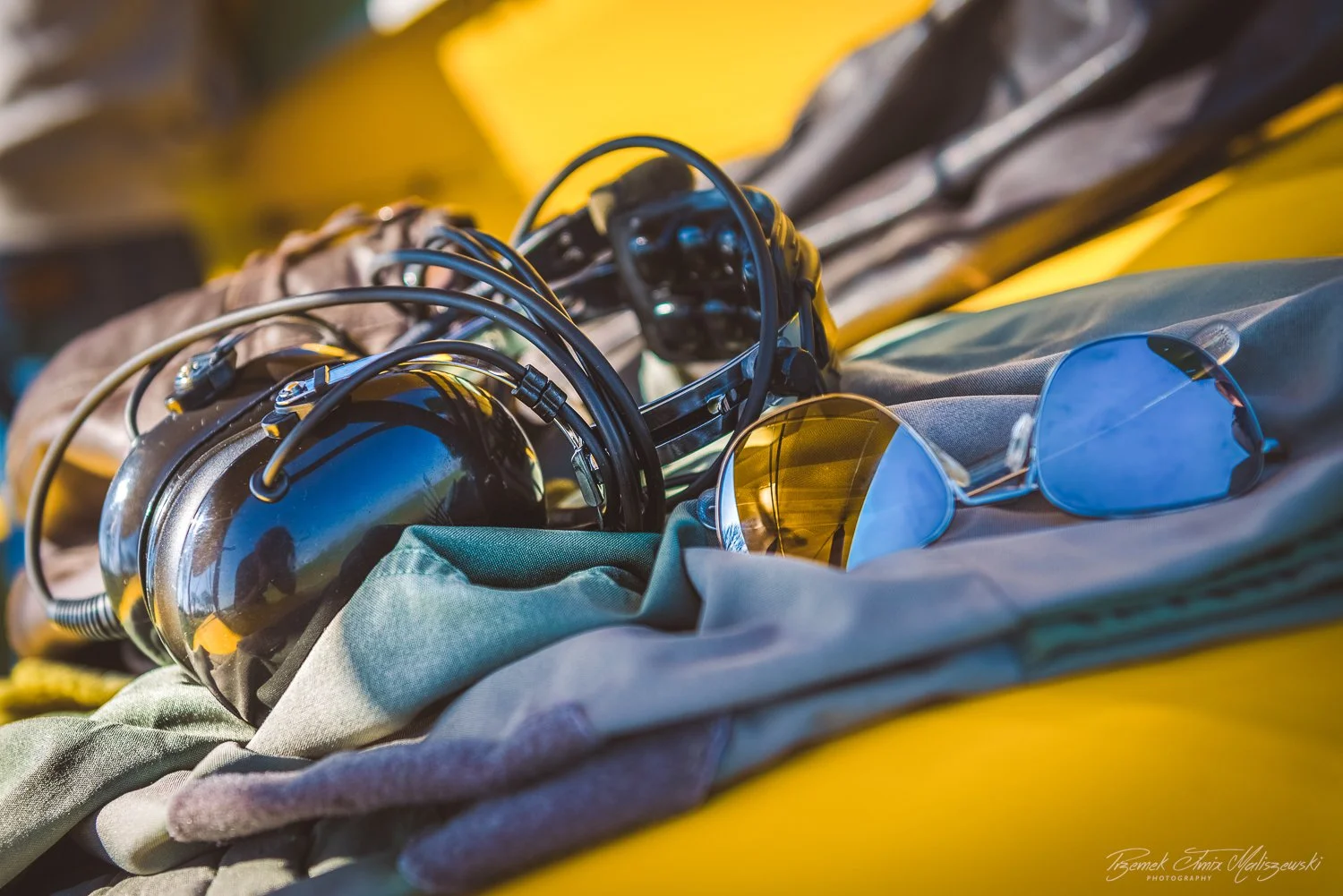 A pair of sunglasses and headphones resting on a fabric surface with a yellow background.