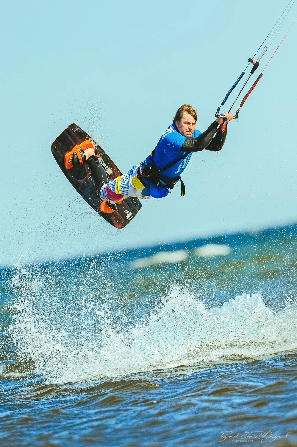 A man performing a jump on a wakeboard over the water, holding onto a kite handle.
