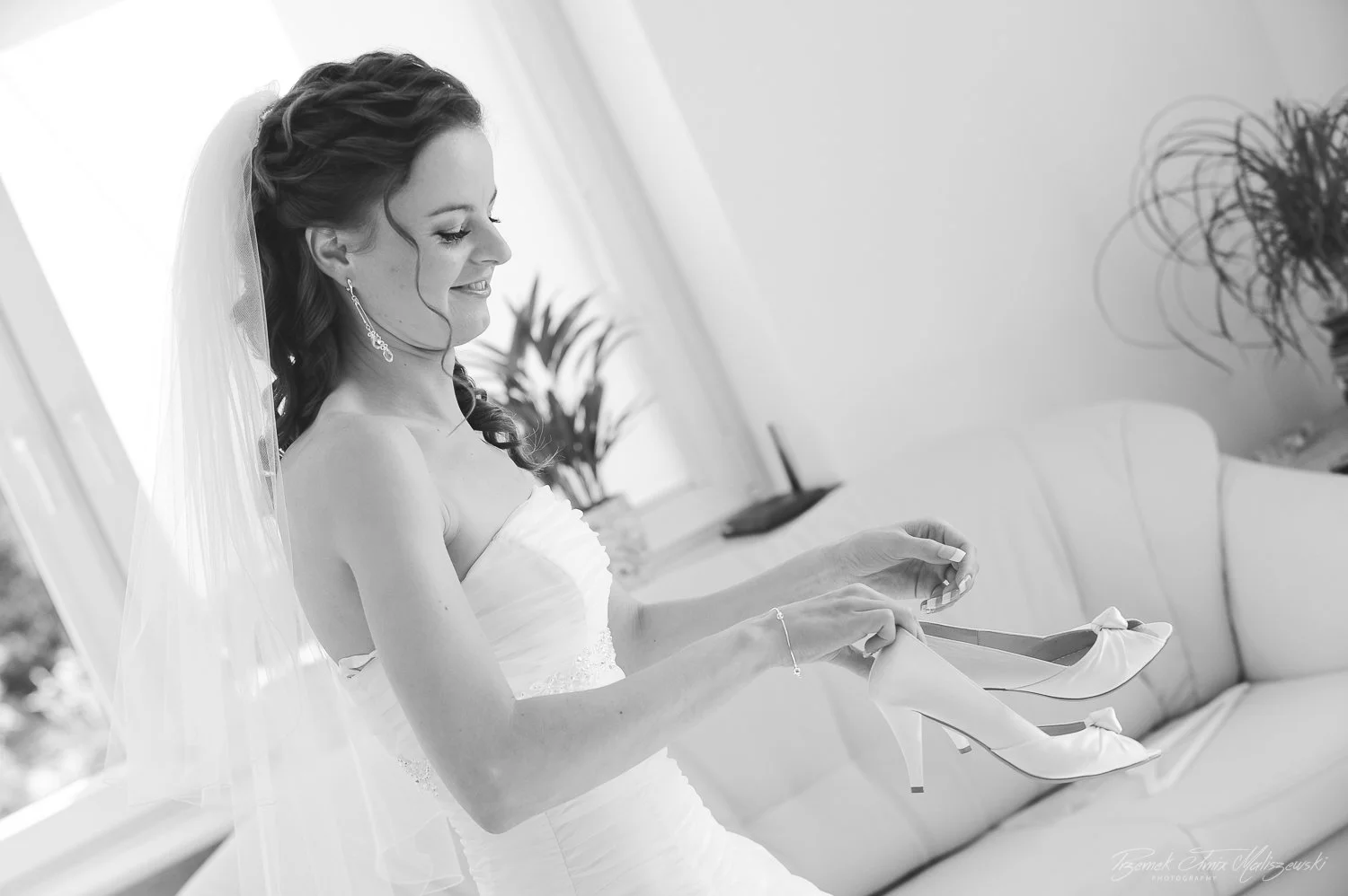 Black and white photo of a bride smiling, holding her wedding shoes.