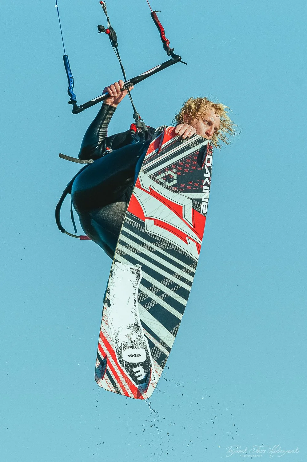 Kiteboarder airborne with a colorful kiteboard in mid-air against blue sky