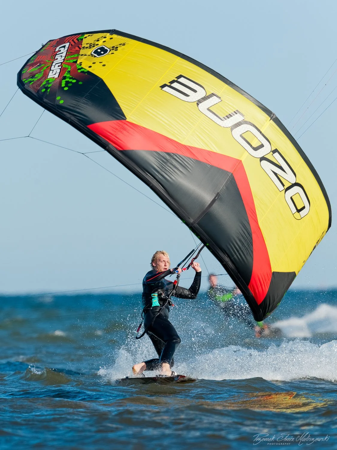 A person kiteboarding on the water with a large yellow, black, and red kite that has the word "NEO" on it.