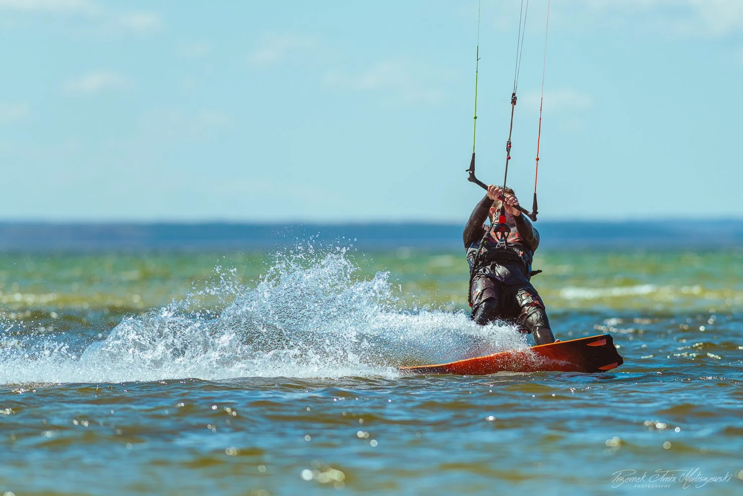 A person in a wetsuit kiteboarding on the ocean, holding onto a control bar with a kite in the sky above the water.