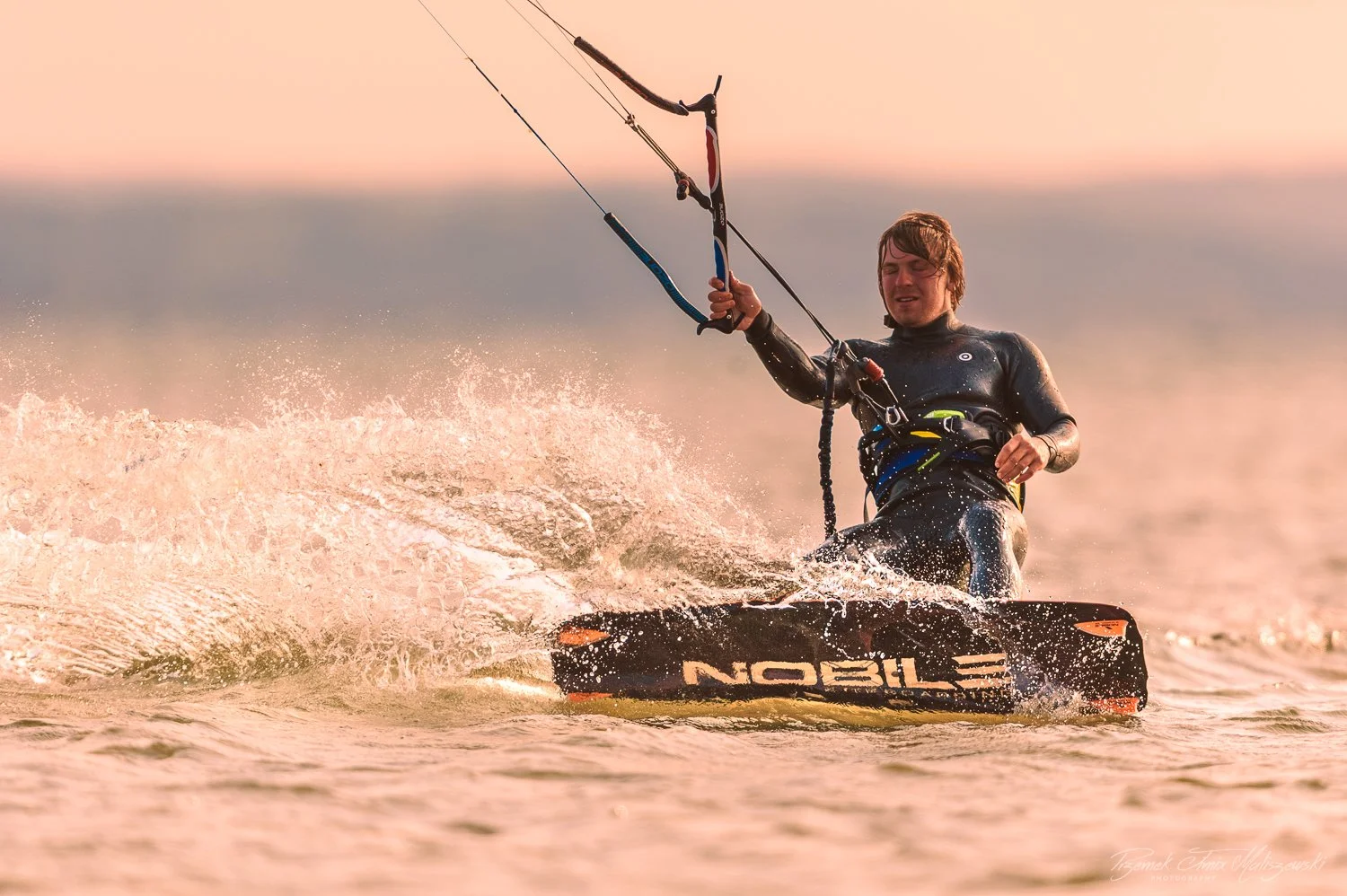 Person kiteboarding on the water during sunset.