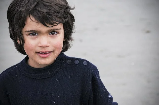 Young boy with dark, curly hair and wearing a dark sweater outdoors.