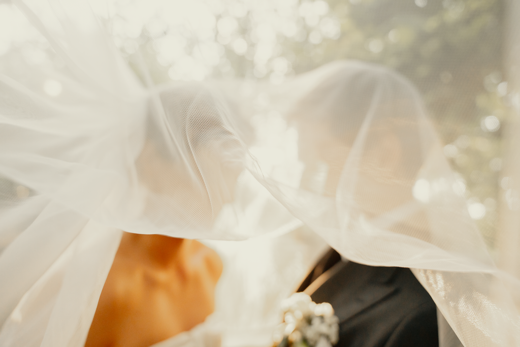 Bride and groom sharing an intimate moment under a wedding veil outdoors.