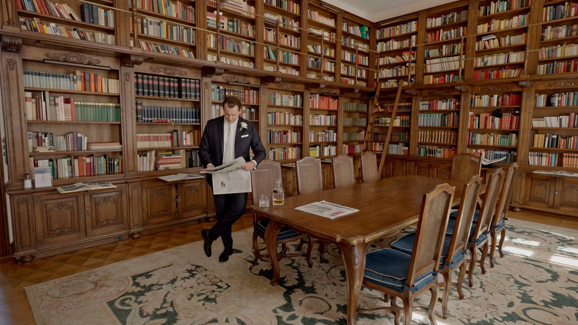 Ein Mann steht in einer großen Bibliothek voller Bücher. Er liest eine Zeitung.