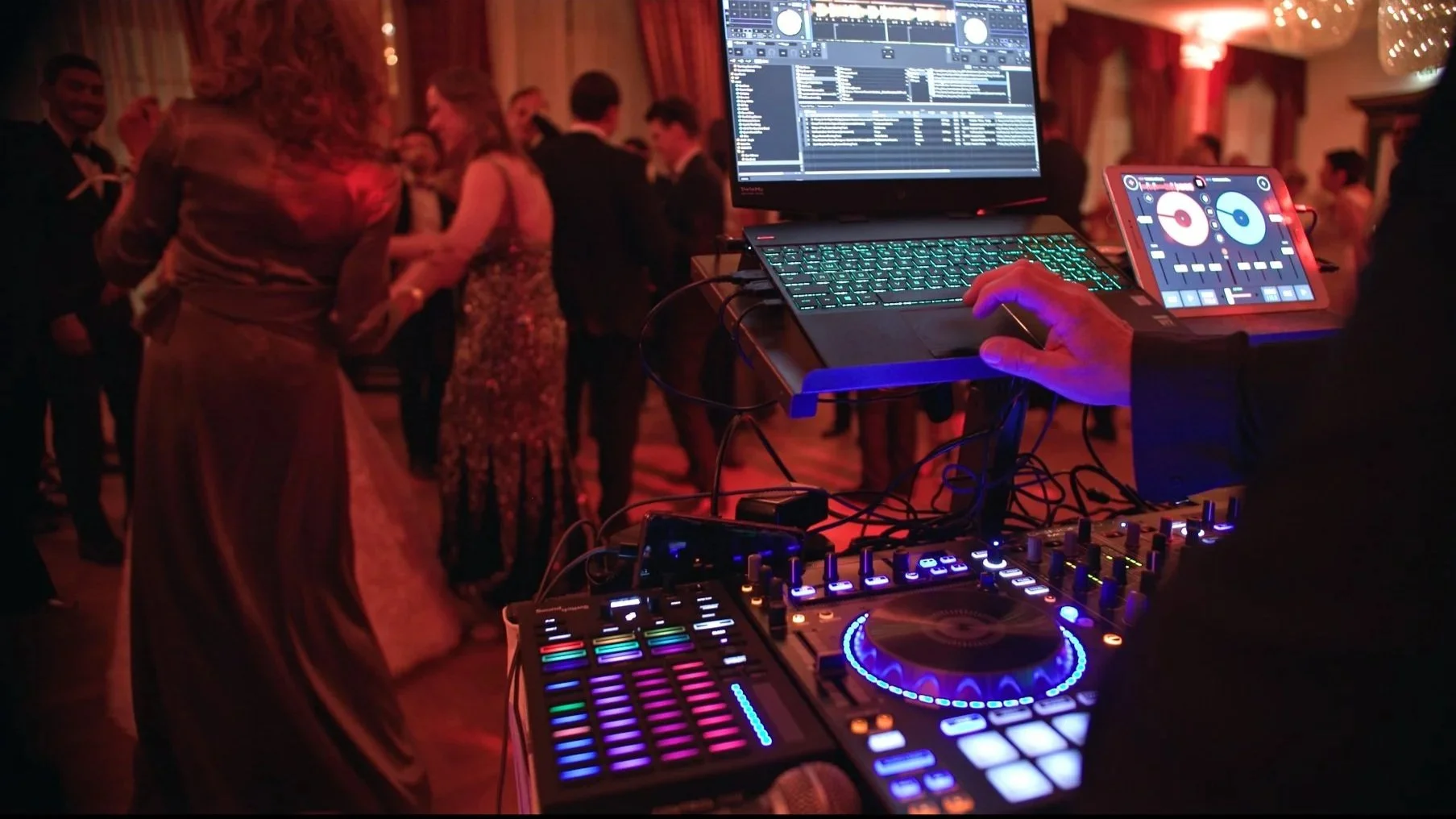 Im Vordergrund spielt ein DJ. Im Hintergrund sehen wir tanzende Leute auf einer Party.