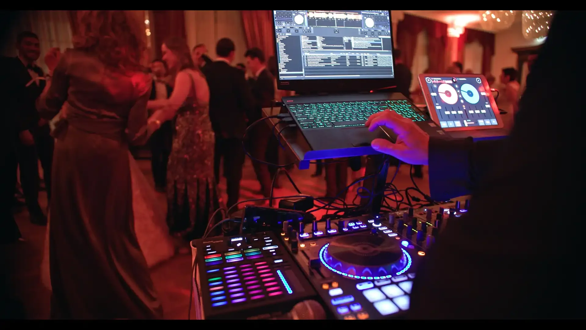 Im Vordergrund spielt ein DJ. Im Hintergrund sehen wir tanzende Leute auf einer Party.