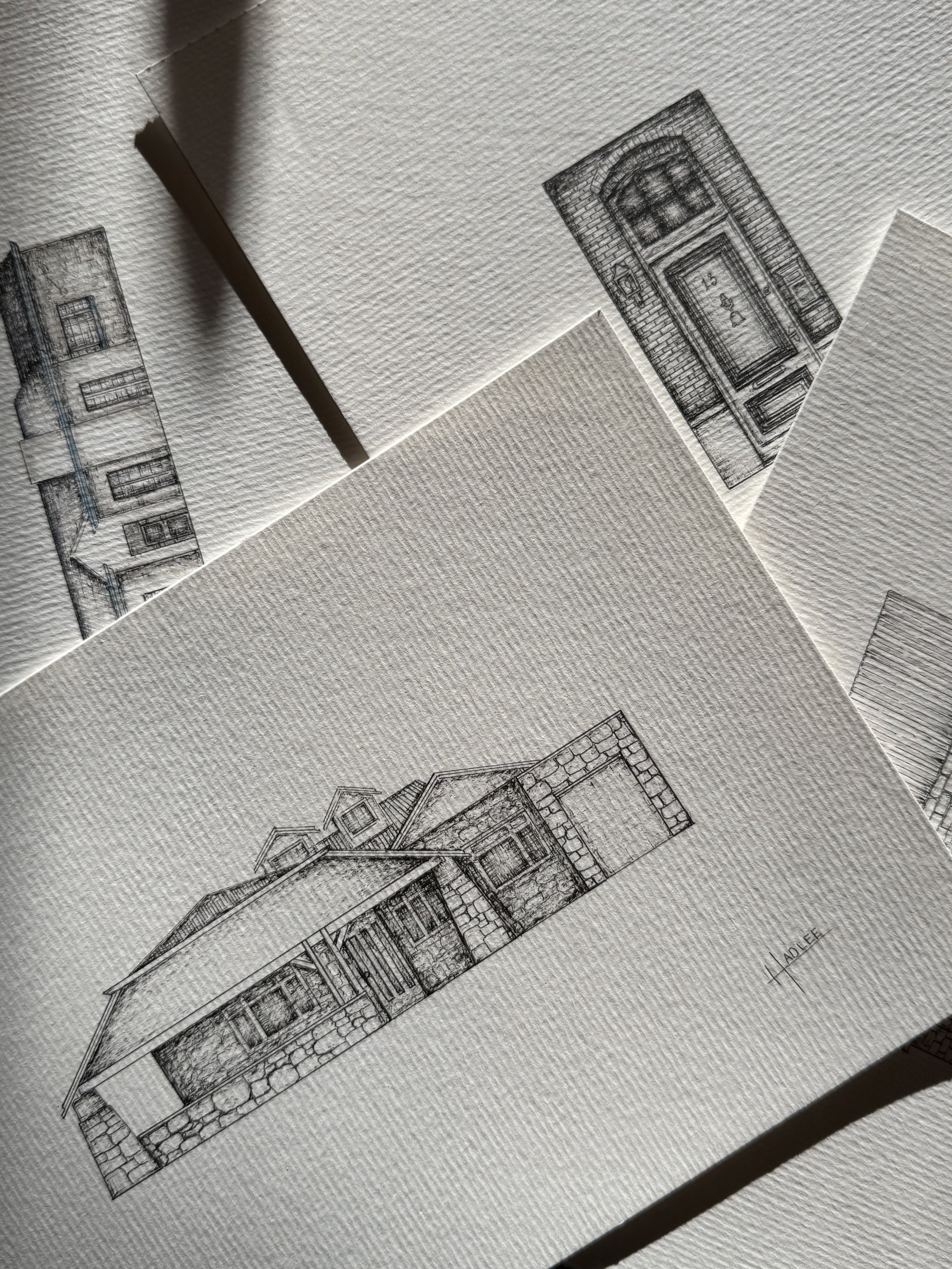 Architectural sketches of house designs on textured paper, with one sketch prominently showing the front view of a house with a gabled roof and stone accents.