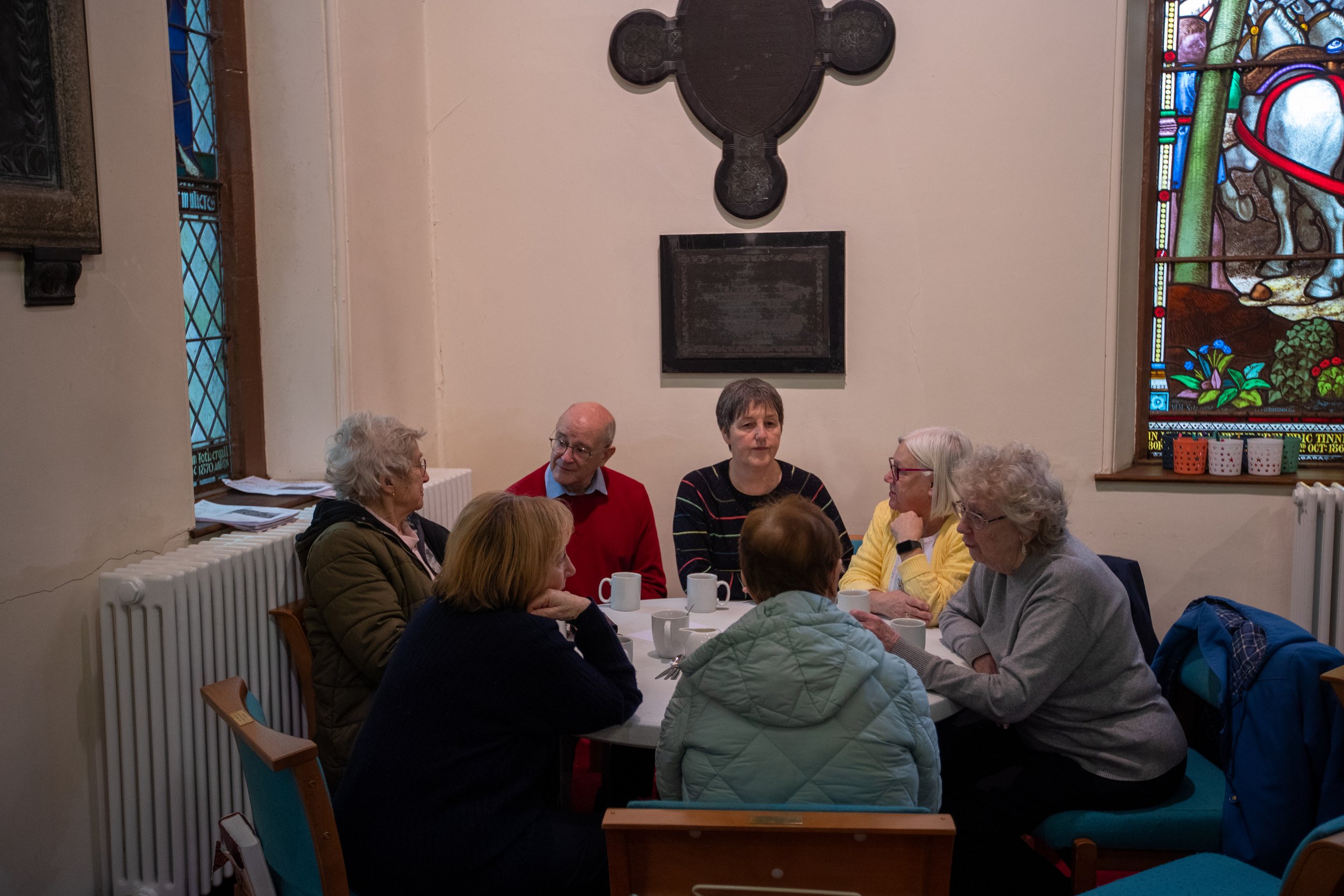 Group of people sitting around a table with mugs talking to each other