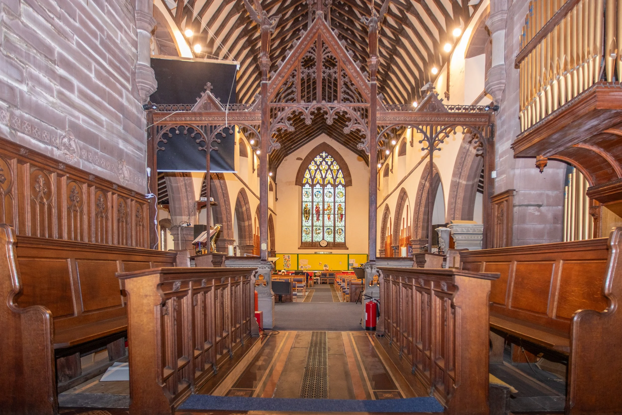 Interior of a church with wooden pews, stained glass window, and decorative wooden altar.