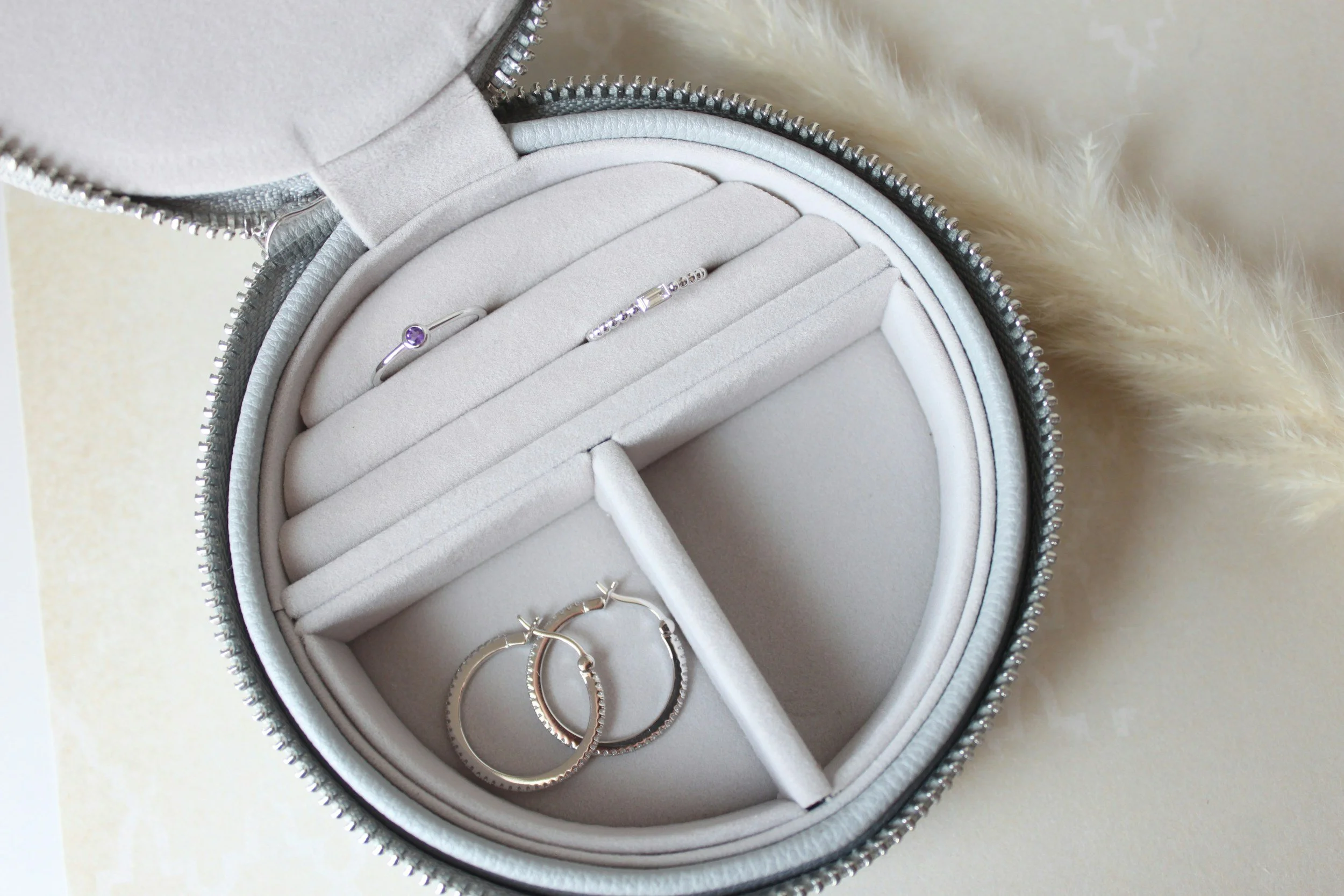 A jewelry box containing a purple gemstone ring, a bracelet, and a pair of gold hoop earrings, on a light-colored surface with a soft furry object nearby.