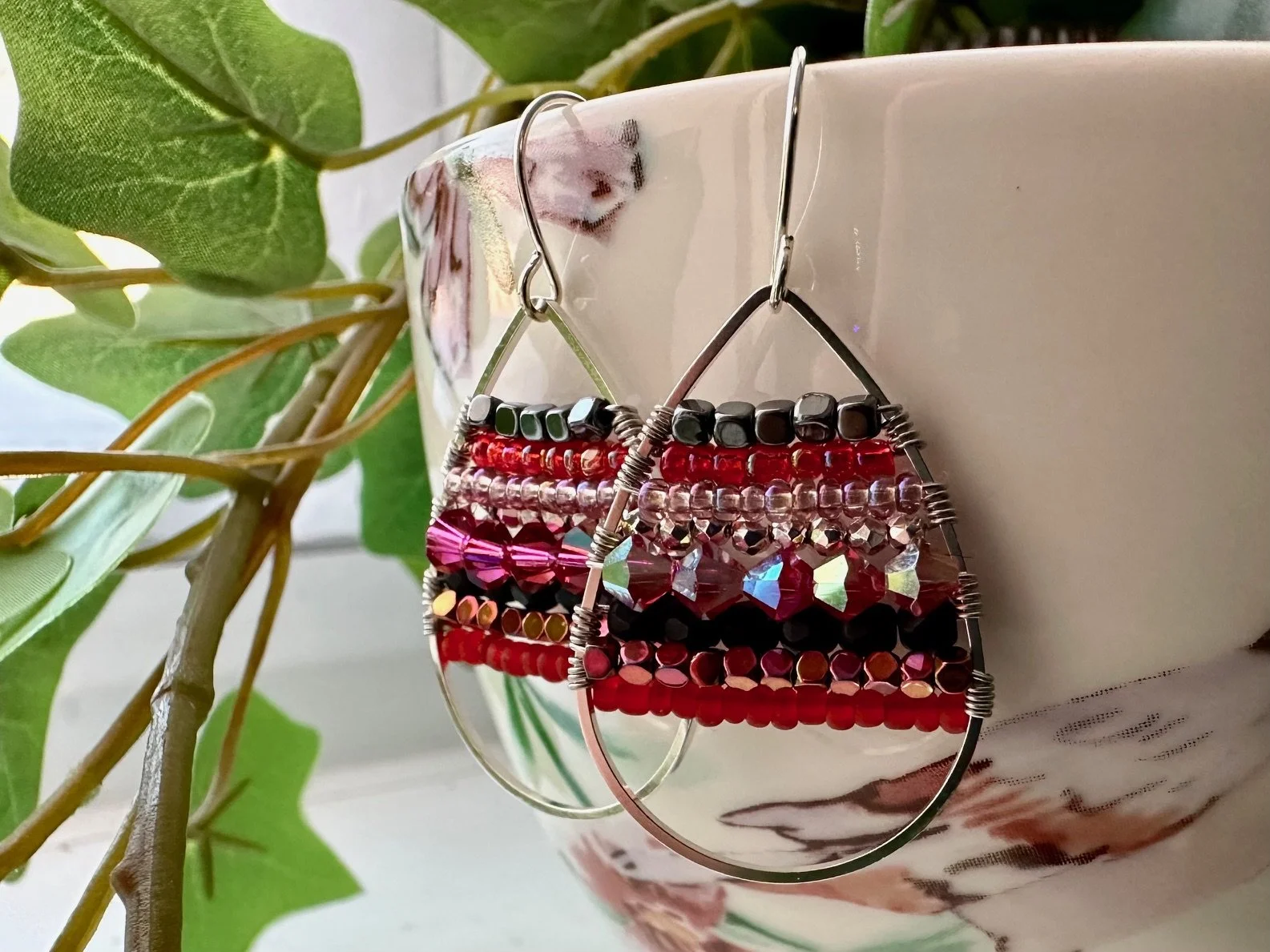 Colorful beaded earrings hanging on the edge of a white ceramic pot beside green leaves.
