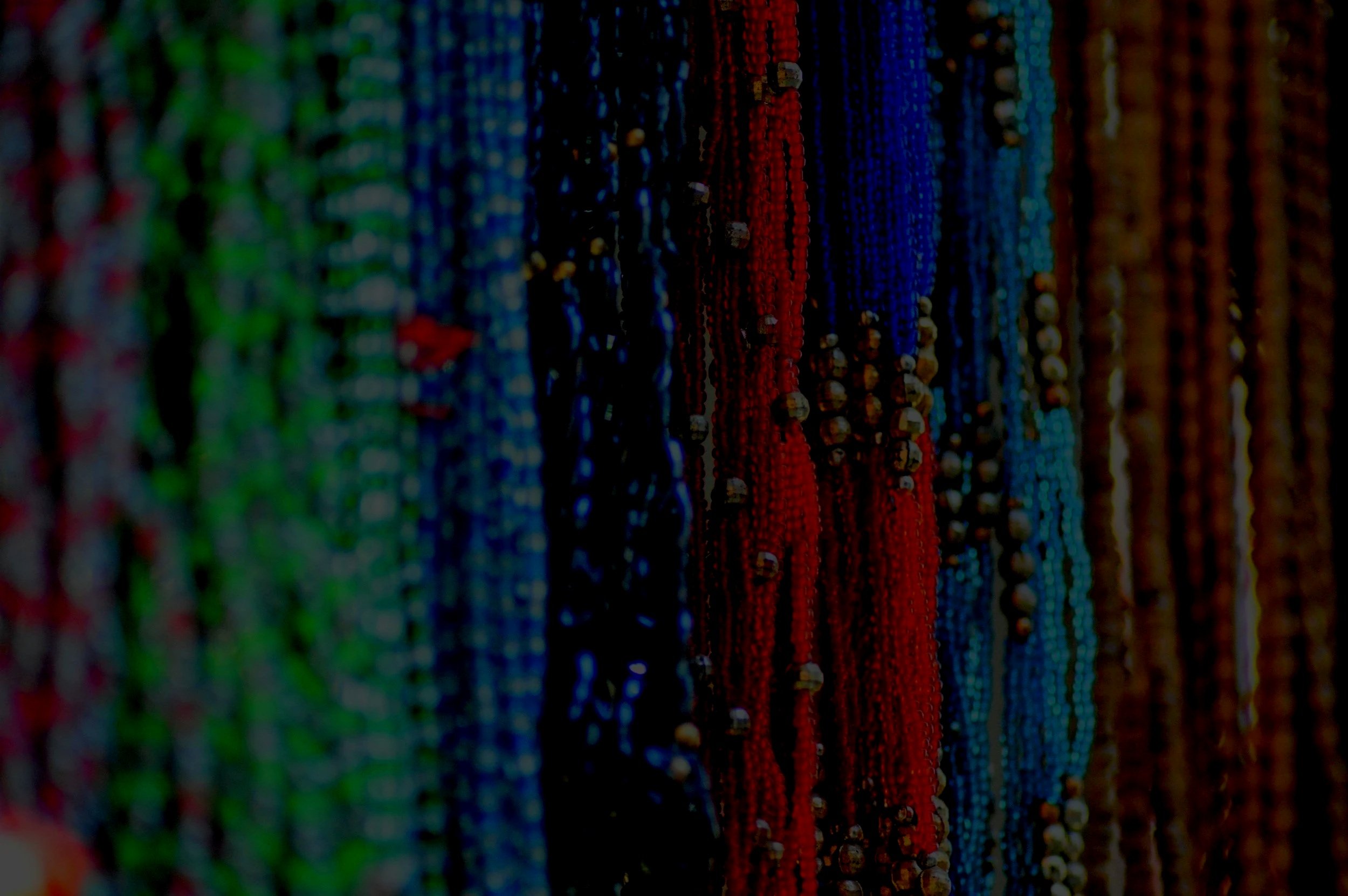 Close-up of colorful beaded necklaces hanging, featuring green, blue, red, turquoise, and brown beads.