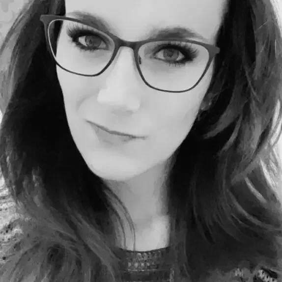 A woman with long, wavy hair wearing glasses and a patterned top.