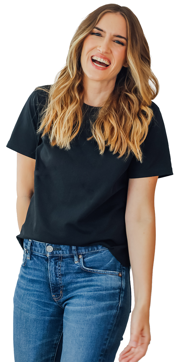 A young woman with long wavy blonde hair laughing and looking directly at the camera, wearing a black t-shirt and blue jeans.