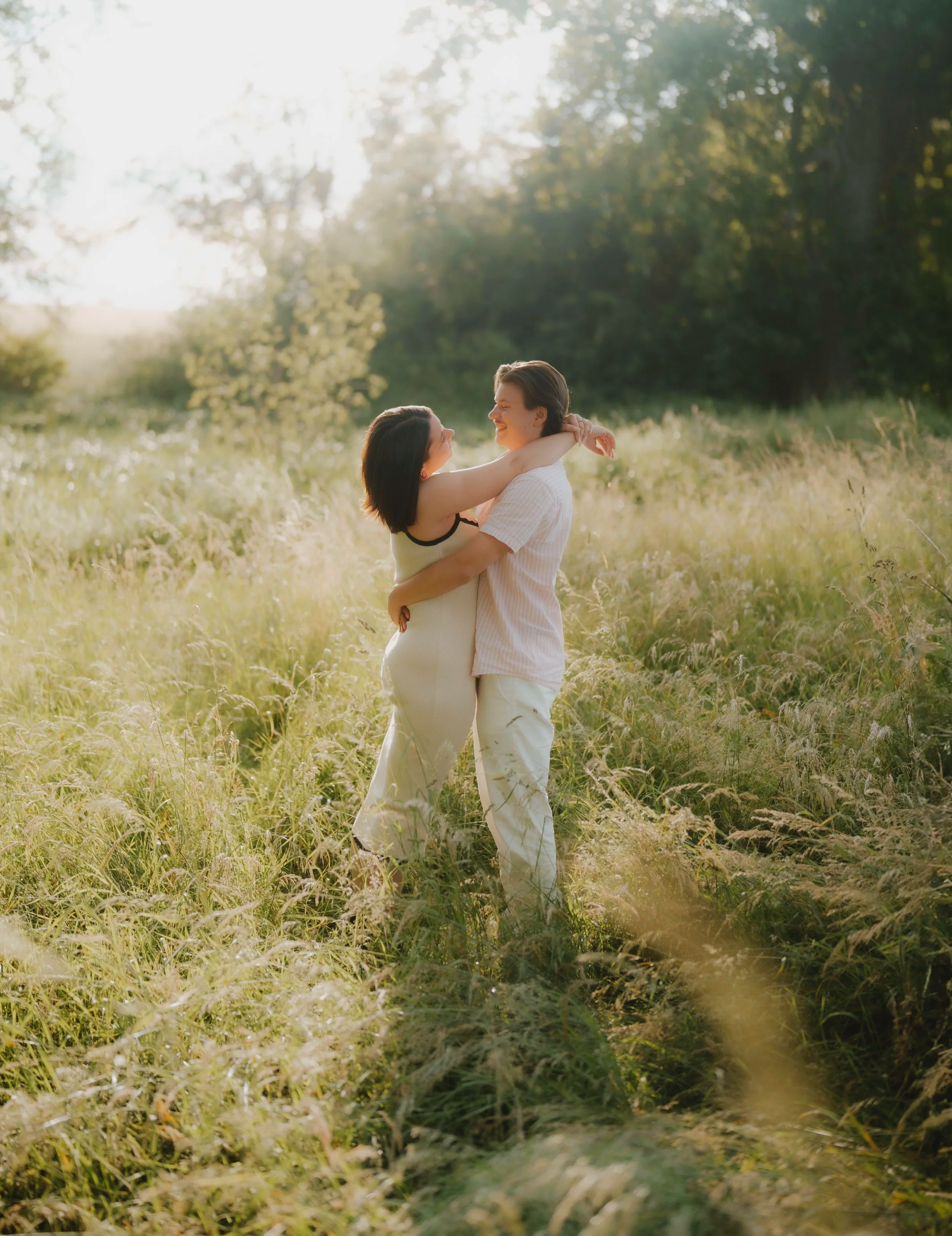 Ein glückliches Paar umarmt sich in einer sonnigen Wiese, umgeben von Pflanzen und Bäumen. Fotografiert von Rebecca Fotografie in Pforzheim.