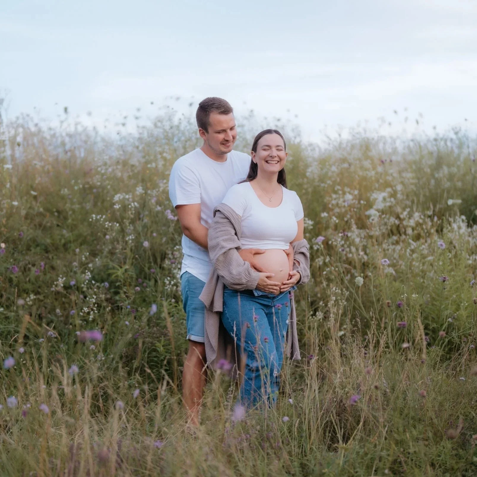 Ein glückliches schwangere Frau mit einem Mann im Freien in einem Blumenfeld. Fotografiert von Rebecca Fotografie in Bretten.
