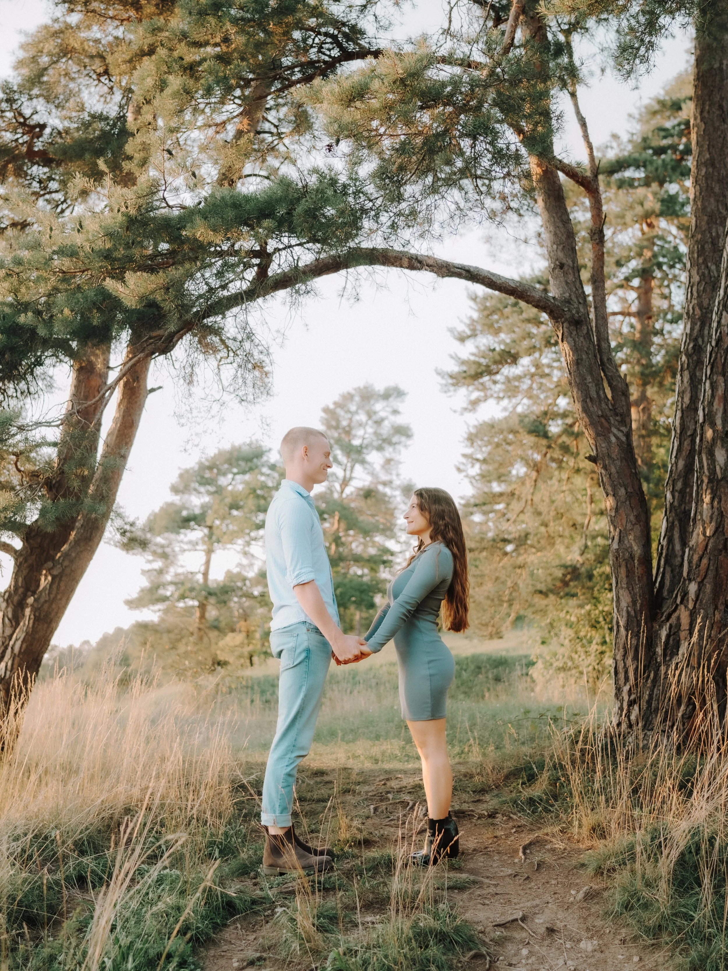 Ein Paar, das sich in einem Wald im Sonnenlicht die Hände hält, umarmt sich und schaut sich lächelnd an. Fotografiert von Rebecca Fotografie in Mühlacker.