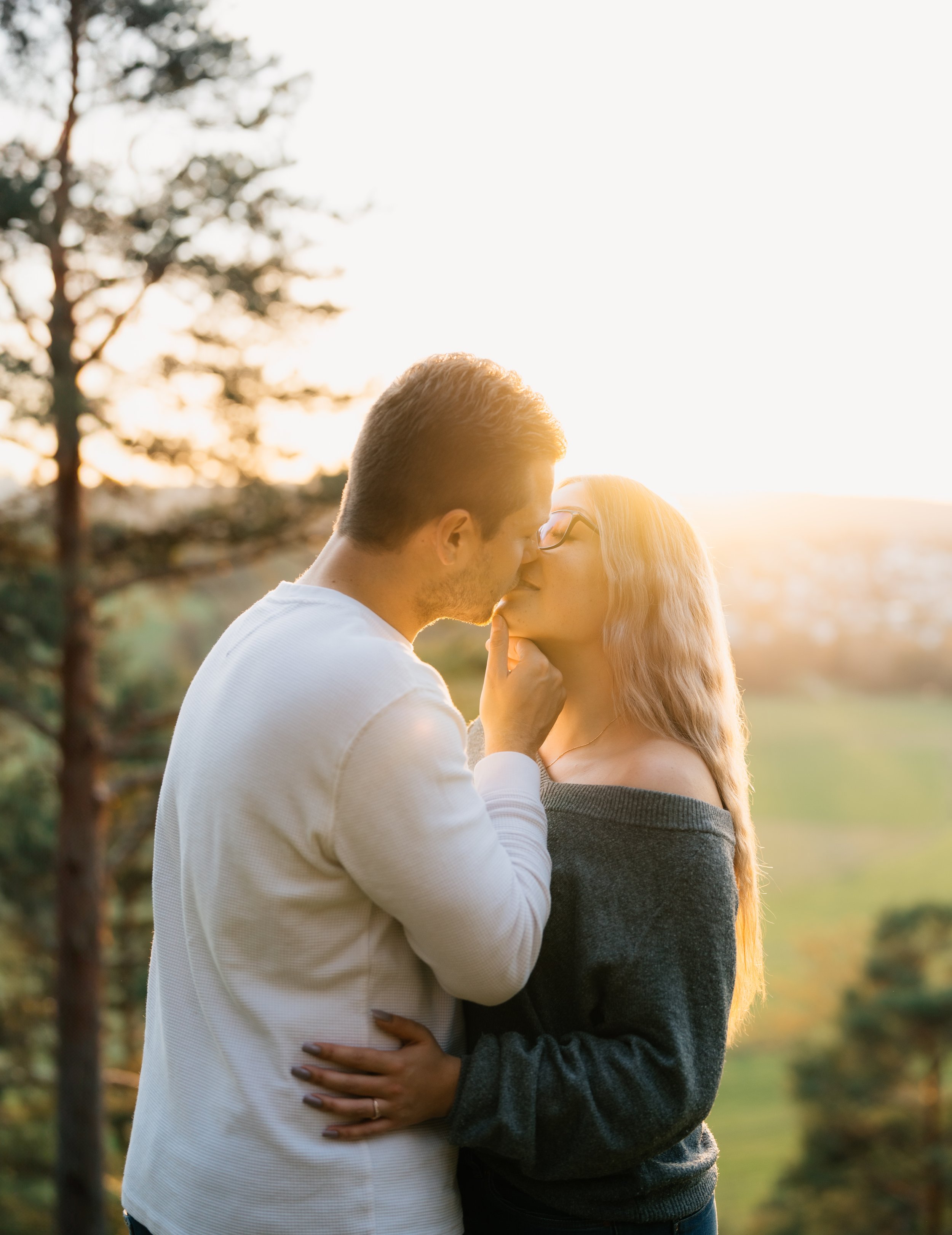 Ein verliebtes Paar küsst sich bei Sonnenuntergang im Freien, umgeben von Bäumen und Natur. Fotografiert in Mühlacker von Rebecca Fotografie.
