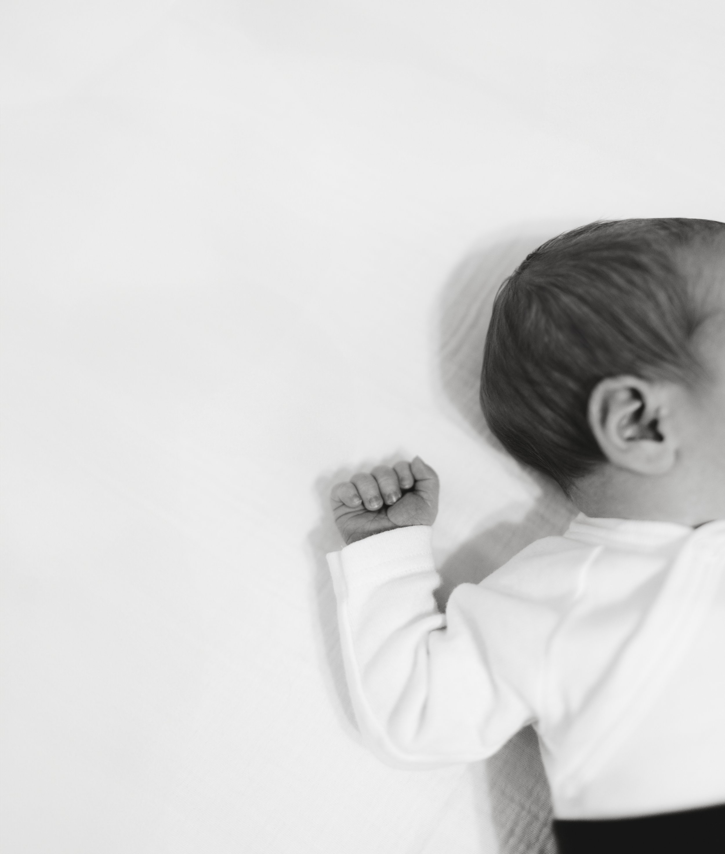 Nahaufnahme eines schlafenden Babys in einem weißen Outfit auf einem weißen Hintergrund, Seiteansicht, Hand in Fäuste. Fotografiert von Rebecca Fotografie.