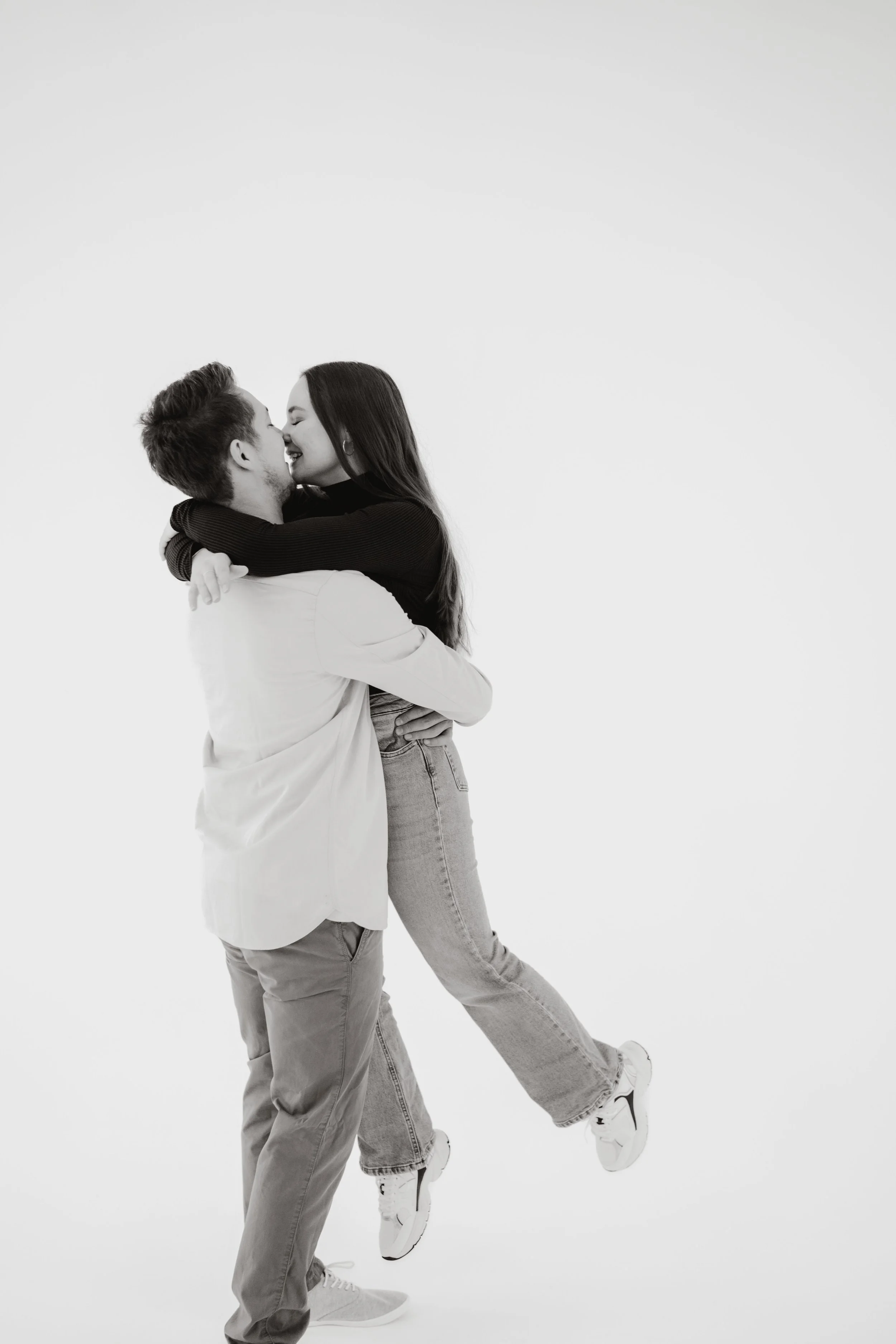 Ein lachendes Paar umarmt sich in einer weißen Kulisse, beide tragen legere Kleidung und Sneakers in einem Fotostudio in Pforzheim. Fotografiert von Rebecca Fotografie.