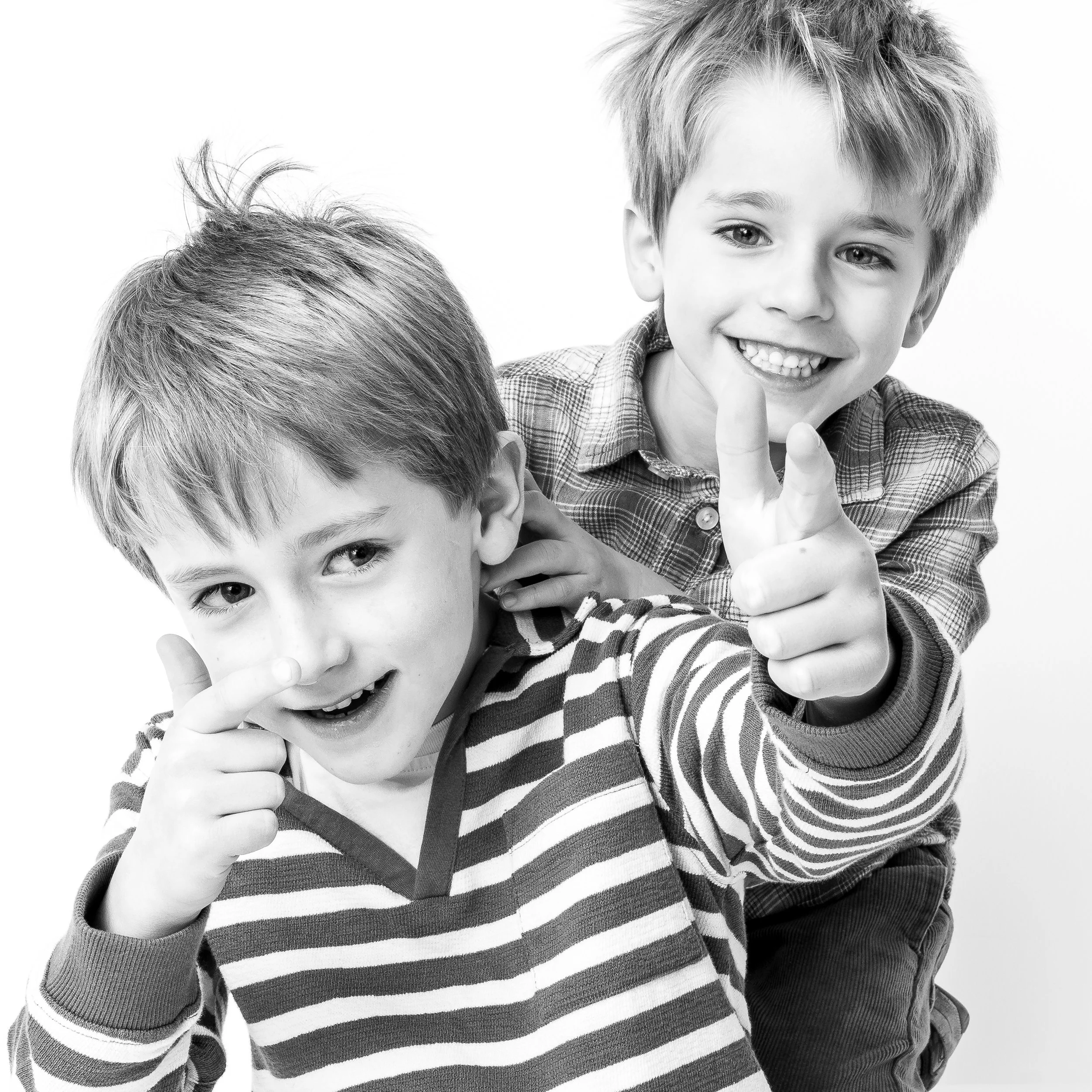 Two young boys playing and smiling at the camera, one pointing finger and the other making a finger gun gesture, in black and white