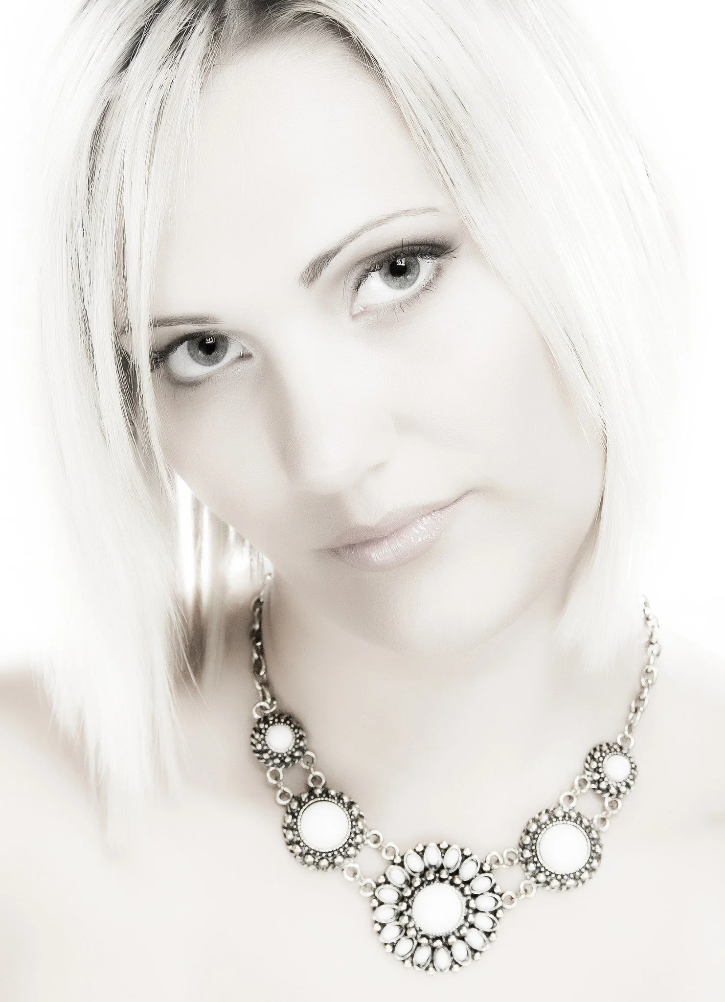 Close-up of a woman with platinum blonde hair and light makeup, wearing a statement necklace with white stones.