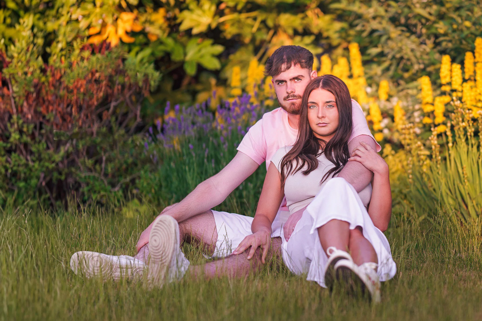 A young couple sitting on grass in a garden with colorful flowers in the background