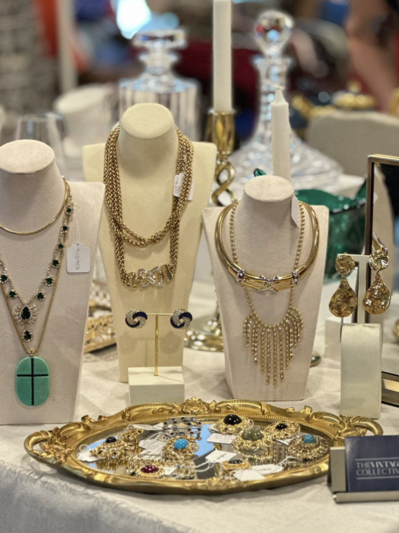 Display of various jewelry including necklaces, earrings, and rings on white bust stands and a decorative gold tray at a jewelry store or market.