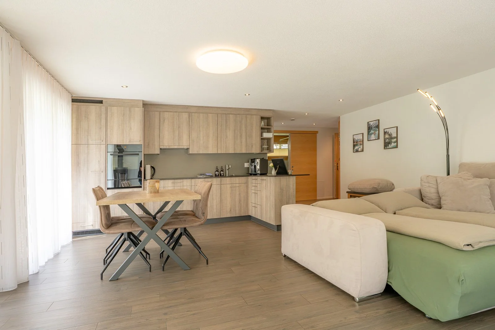 Offene Wohnküche mit Esstisch, Blick auf Sofa und dekorative Wandbilder.