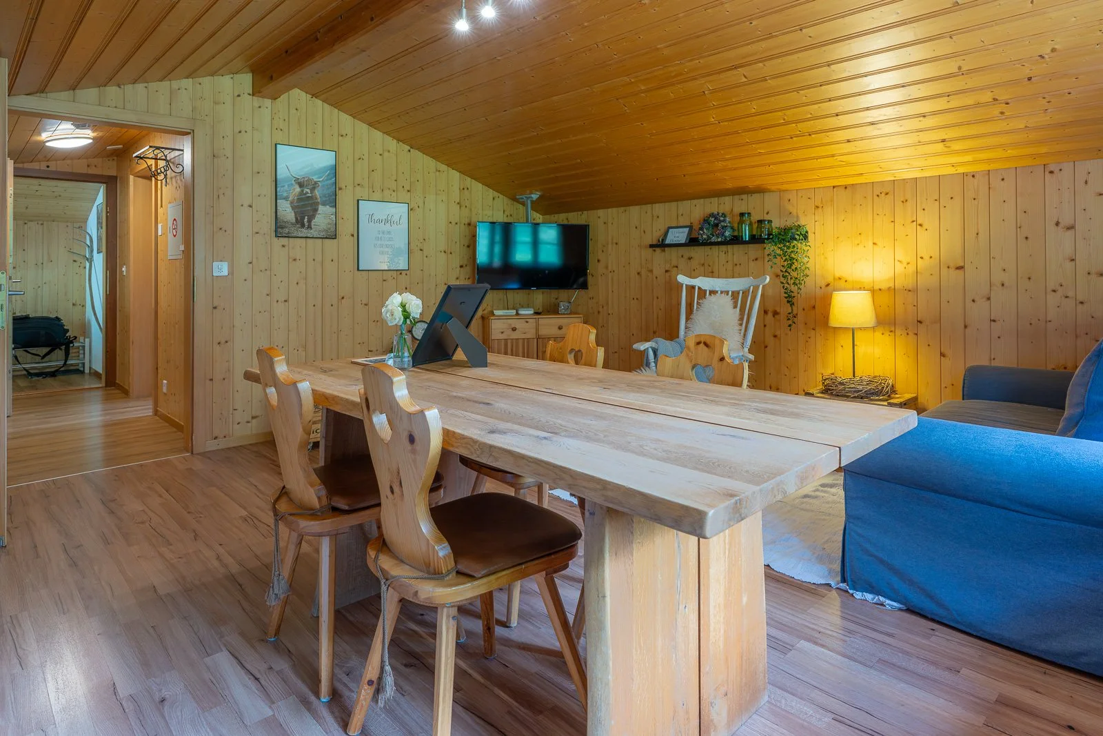 Holzverkleideter Wohnbereich mit Esstisch, Fernseher, Sessel, Couch und Dekorationsgegenständen in einer gemütlichen, rustikalen Umgebung.