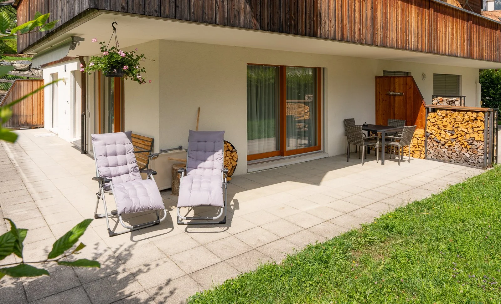 Balkon mit zwei Liegen, einem Esstisch mit vier Stühlen, Holzschnitt und Holz feuertöpfen, und einer blühenden Pflanze.