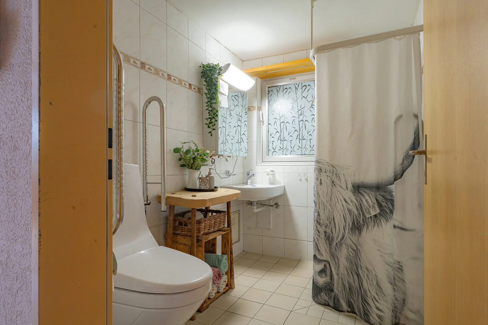 Kleines Badezimmer mit Toilette, Waschbecken, Fenster, Spiegel, Pflanzen und Duschvorhang mit Löwenmotiv