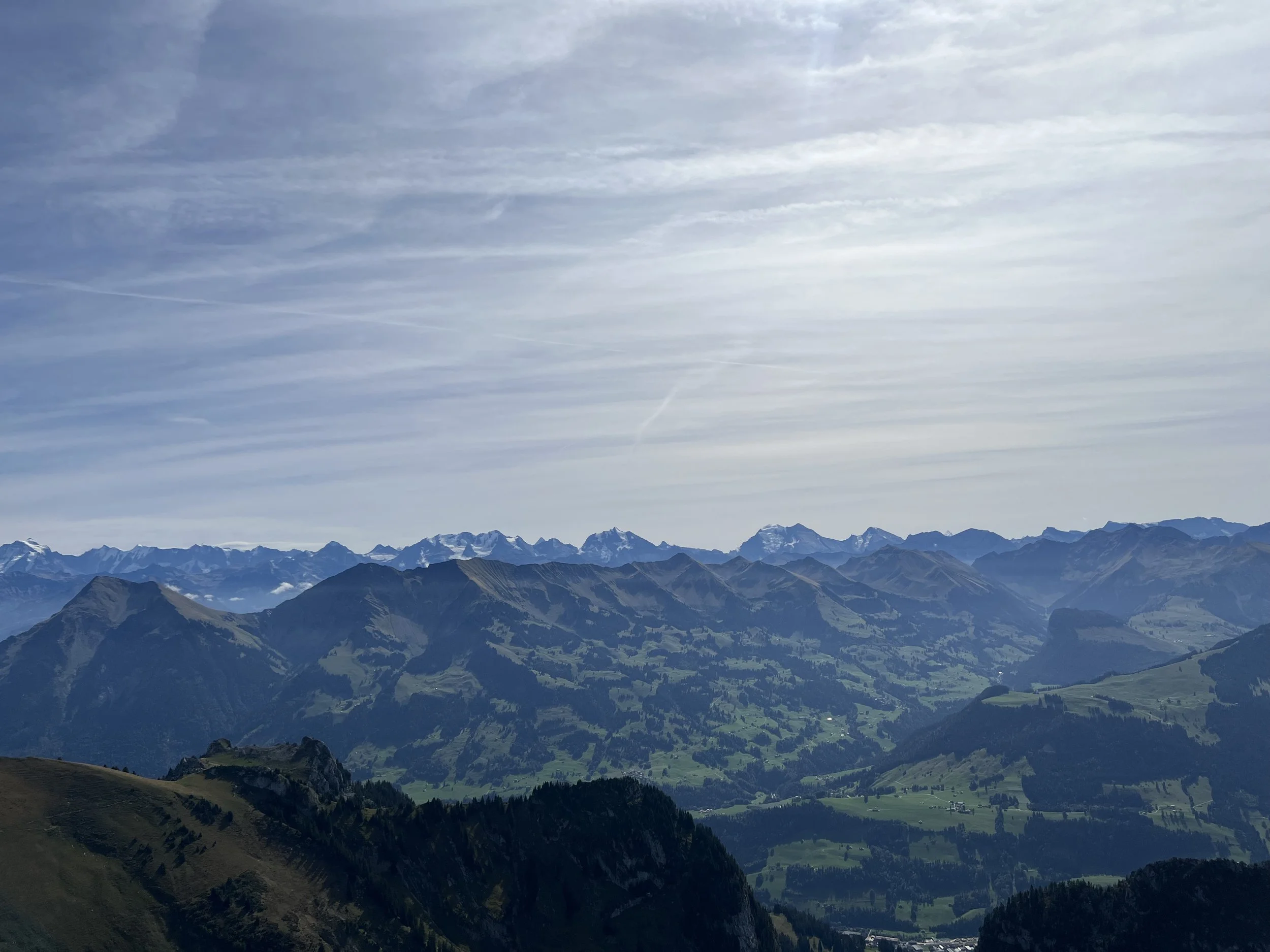Panoramablick auf eine alpine Berglandschaft mit grünen Tälern, schroffen Gipfeln und schneebedeckten Bergen unter bewölktem Himmel