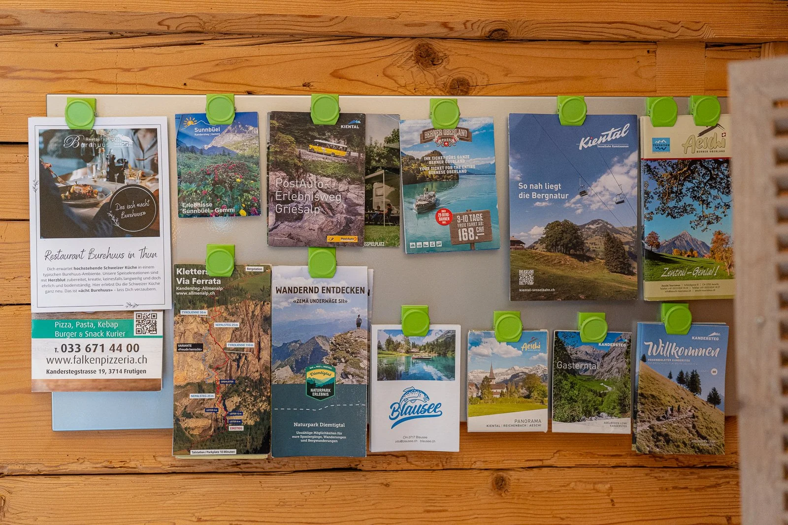 Eine Pinnwand mit verschiedenen Werbe- und Informationsbroschüren für Tourismus und Gastronomie im Kanton Thun, Schweiz, auf einem Holzbrett befestigt.