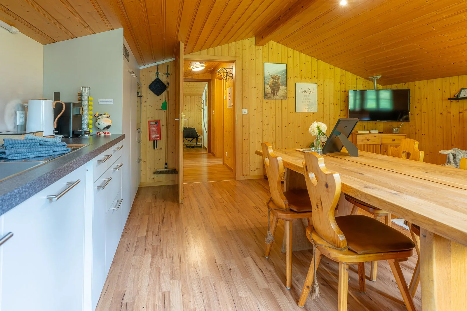 Ein gemütliches Wohnzimmer mit Holzverkleidung, einem großen Esstisch, Stühlen, einem Fernseher und einer kleinen Küchenzeile.
