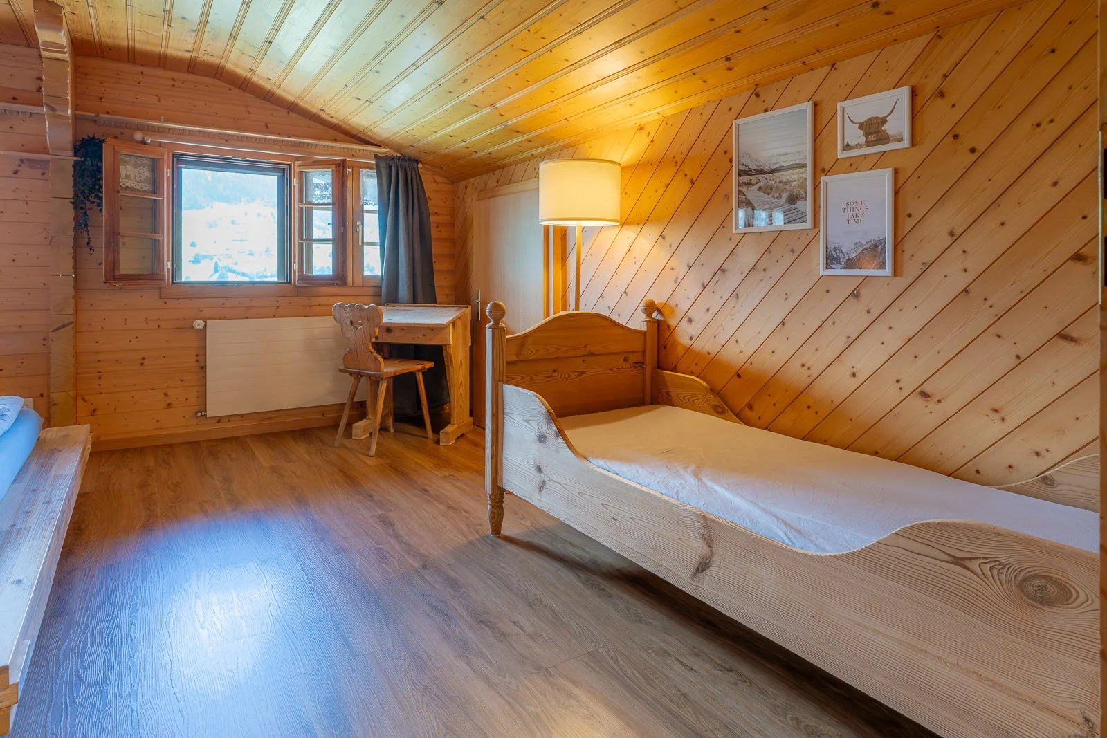 Gemütliches Schlafzimmer mit Holzvertäfelung, Einzelbett, Schreibtisch, Stuhl, Stehlampe, Wanddekorationen und Fenster mit Blick nach draußen.