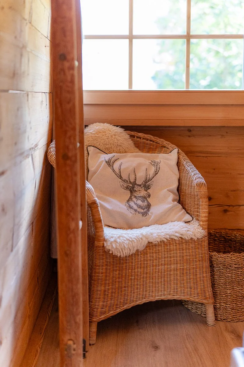Ein Korbbett mit einem Kissen mit einem Hirschkopf-Design, auf einem Raum aus Holz mit einem Fenster im Hintergrund.
