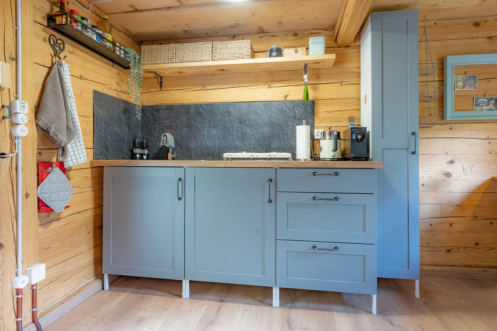 Küche in einem Holzhaus mit blauer Schrankküche, schwarzen Regalen, verschiedenen Küchenutensilien und dekorativen Elementen.