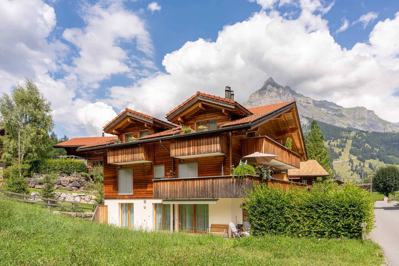 Ein zweistöckiges Holzhaus in den Bergen mit Garten, Balkon und umliegender Natur.
