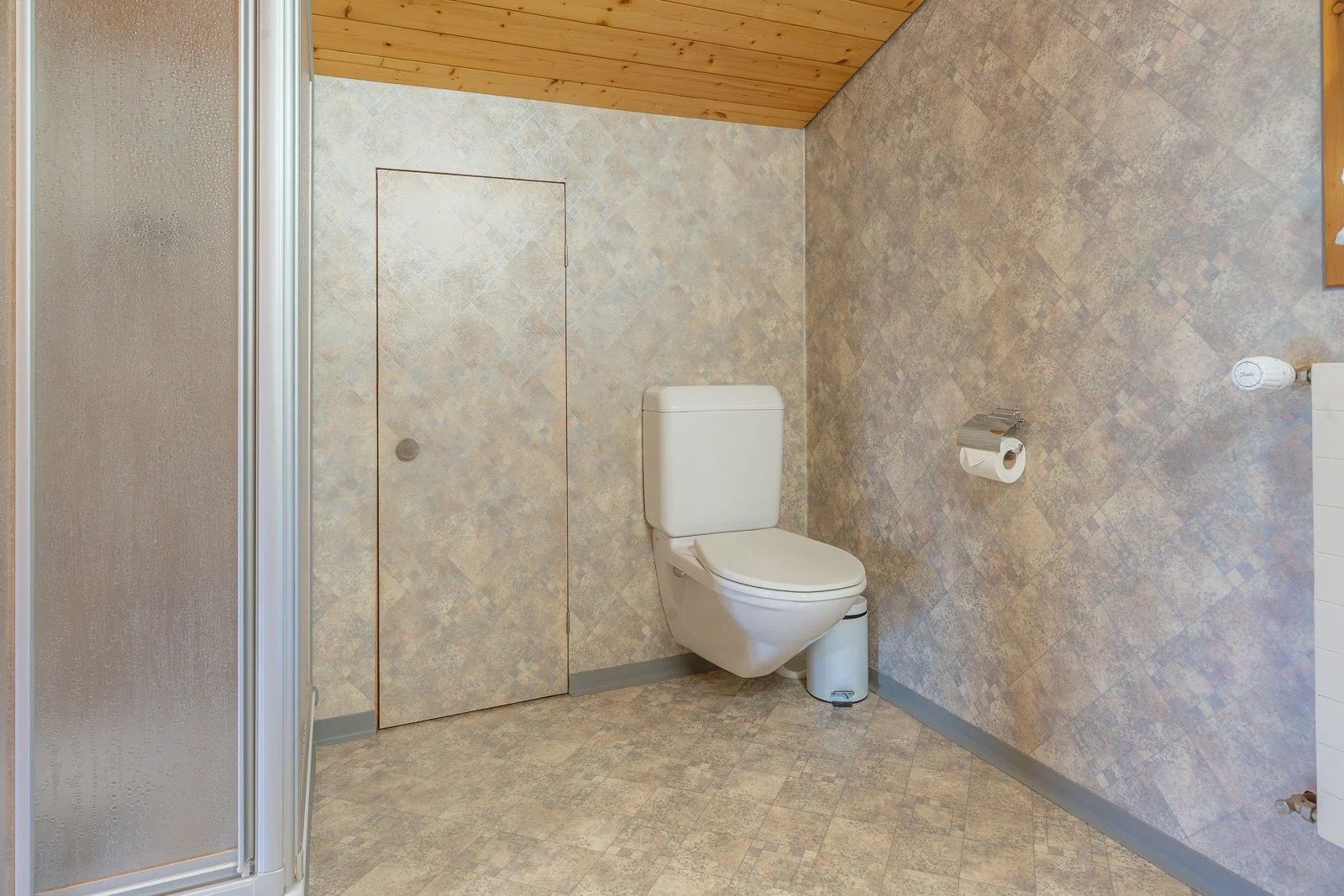 Badezimmer mit Toilette, Toilettenpapier, Duschkabine und Holzdecke.