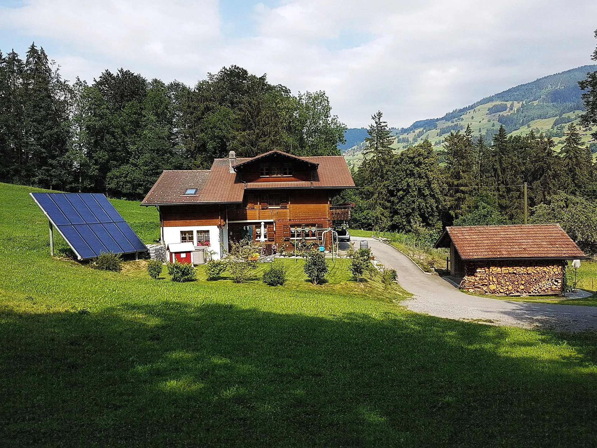 Ein Haus in einer ländlichen Gegend, umgeben von Bäumen und Bergen im Hintergrund.