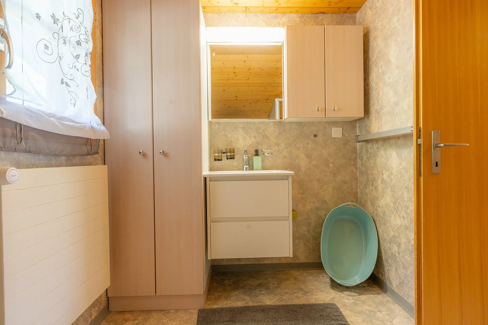 Kleines Badezimmer mit Waschbecken, Spiegel, Badezimmerschrank, Wäschetrockner, blaue Wanne, Holzdecke und Holztür.