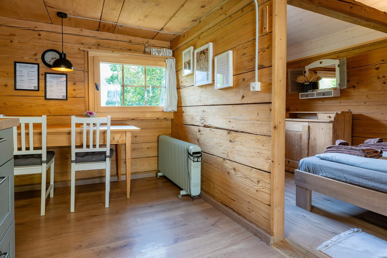 Innenansicht eines Holzhauses mit Essbereich und Schlafzimmer. Holzwände, Fenster, TV, Bett, Schrank, Dekorationen.