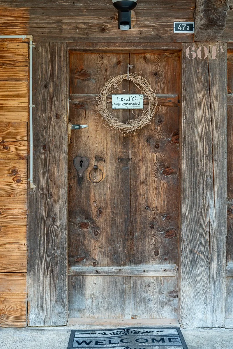 Eine hölzerne Eingangstür mit Willkommen-Schild und Naturkranz
