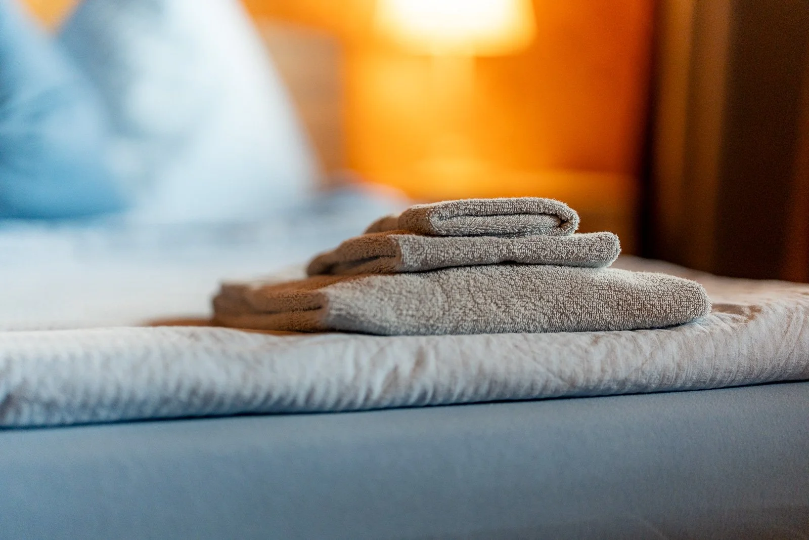 Faltende Handtücher auf einem Bett, im Hintergrund warmes Licht