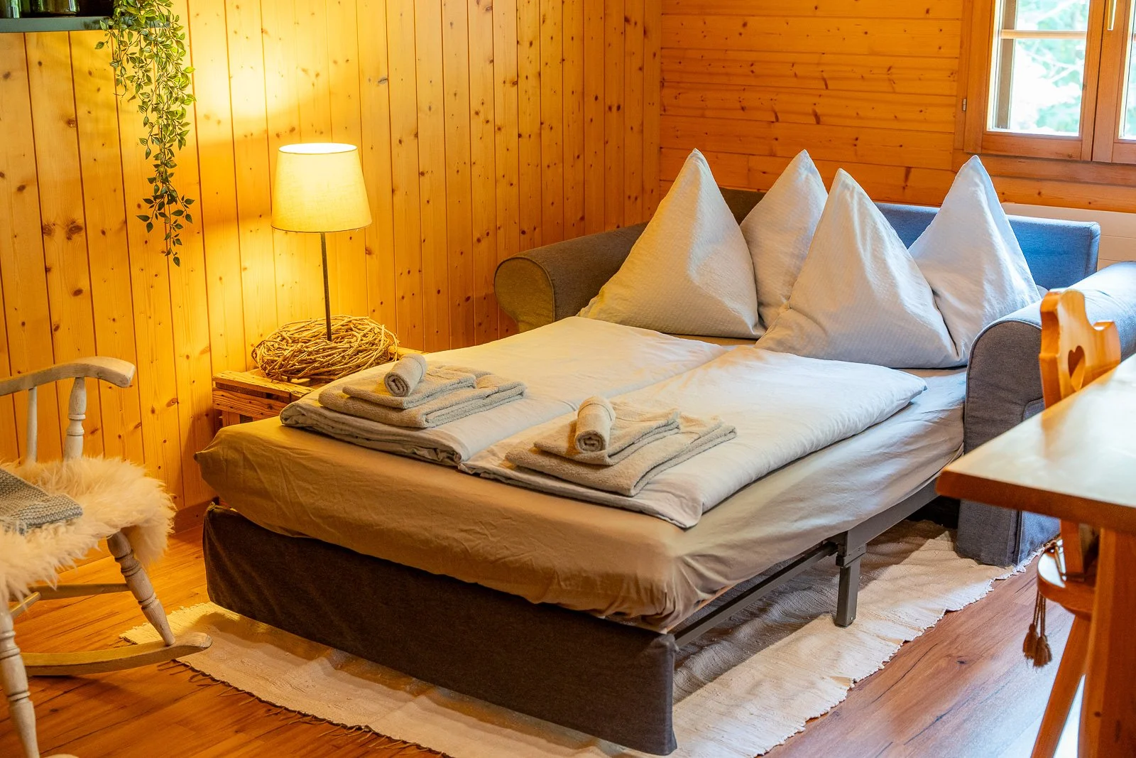 Bett in einem Holzzimmer mit weißen Kissen, Handtüchern und einer Lampe auf einem Nachttisch.